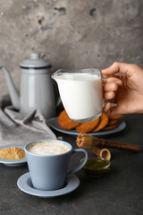 Female hand with jug of milk and cup of hojicha latte on dark background, closeup