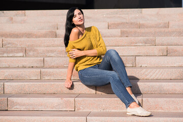 Beautiful and attractive caucasian brunette girl in a yellow sweater posing while sitting on the steps.