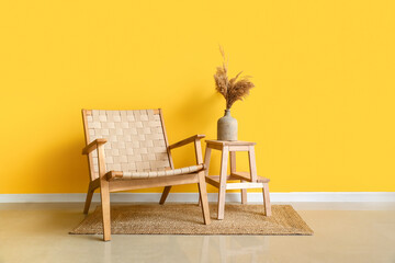 Modern armchair and step stool with vase near yellow wall