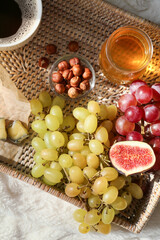 Tray with sweet grapes, fig, honey and hazelnuts on plaid, closeup