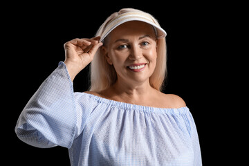 Smiling mature woman in visor cap on dark background