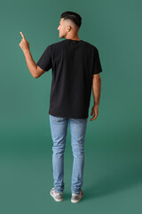 Handsome young man in stylish t-shirt pointing at something on color background, back view
