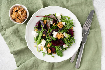Healthy beet salad with feta and walnuts served on white plate, table top view