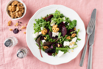 Healthy beet salad with feta and walnuts served on white plate, table top view
