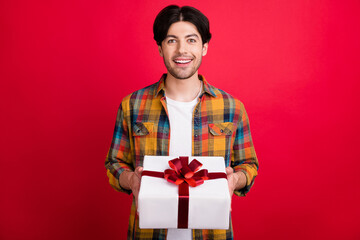 Photo of adorable excited young gentleman wear plaid outfit smiling holding present box isolated red color background