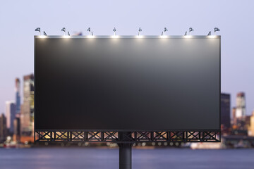 Blank black billboard on city buildings background at night, front view. Mockup, advertising concept