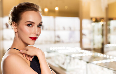 Obraz na płótnie Canvas luxury and people concept - beautiful woman with red lips in black dress over jewelry store background