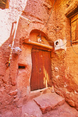 The old wooden curved door at the corner of medieval house, covered with red-ochre mud, Abyaneh,...