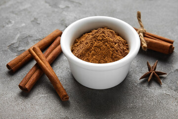 Bowl with cinnamon powder and sticks on dark background