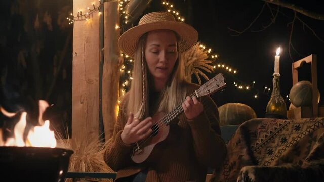 Girl in a hat plays the ukulele and sings by the campfire