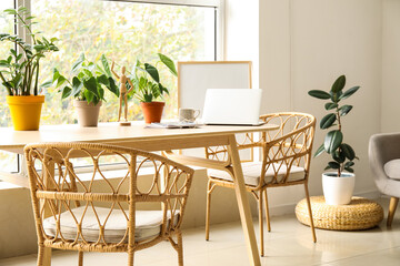 Wooden table with laptop and houseplants in interior of living room