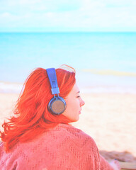 Redhead sexy woman listening to music on the beach. Amazing woman on break in sunbathes on the coast, and listens to relaxing music. Wrap the person in a warm blanket.