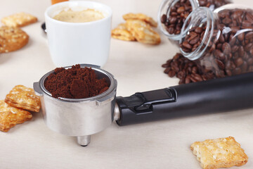 Cup of espresso, crackers, holder with ground coffee and cans of coffee beans on table.