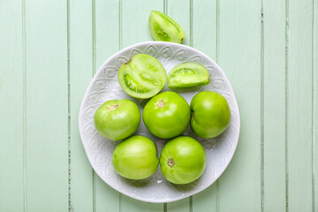 Plate with green tomatoes on color wooden background
