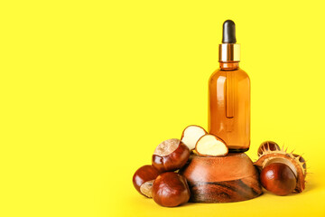 Bottle of essential oil and fresh chestnuts on yellow background