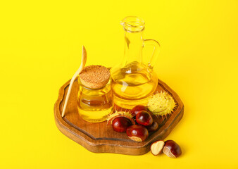 Obraz na płótnie Canvas Wooden board with essential oil and chestnuts on yellow background