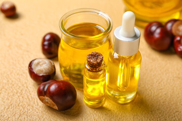 Bottles with essential oil and chestnuts on color background, closeup