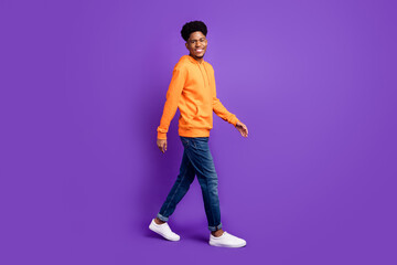 Full body photo of happy afro american positive man walk empty space smile isolated on purple color...