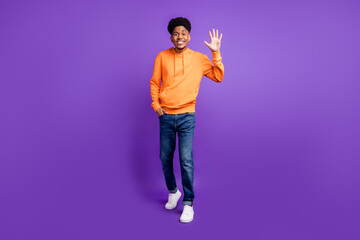 Full body photo of young black man happy positive smile waving hand hello hi isolated over violet color background © deagreez