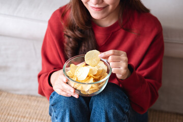 Closeup image of a young woman picking and eating potato chips at home