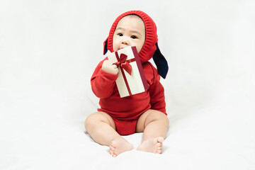Happy infant asian baby boy toddler in red bodysuit holding gift box sitting on white background.Concept holiday Christmas, happy new year, infants, childhood.