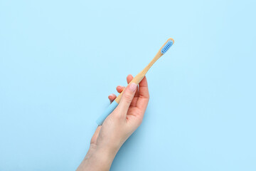 Female hand with wooden toothbrush on blue background