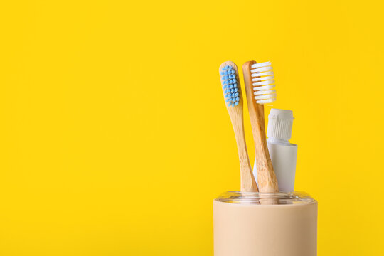 Holder with wooden toothbrushes and paste on yellow background, closeup