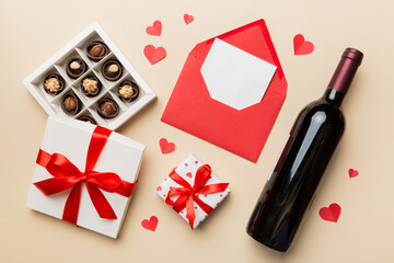 Bottle of red wine on colored background for Valentine Day with gift box, envelope and chocolate. Heart shaped with gift box of chocolates top view with copy space