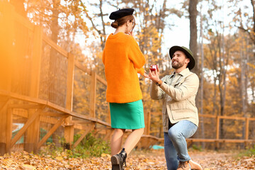 Naklejka na ściany i meble Handsome man proposing to his beloved in beautiful autumn park