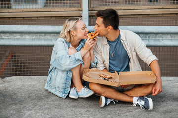 summer holidays, food and people concept - happy young couple eating takeaway pizza on city roof...