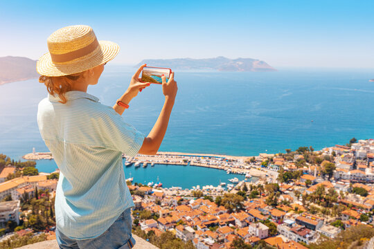 Tourist girl taking photos on smartphone of the scenic landscape of mediterranean resort town. Sightseeing and travel blogger concept