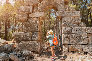 Fototapeta na wymiar Traveler girl walks through the ancient ruins and arches of the antique Greek city of Phaselis in Turkey. Historical sightseeing and archeology concept