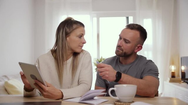 Caucasian couple sitting at home typing on digital tablet sorting out finances 