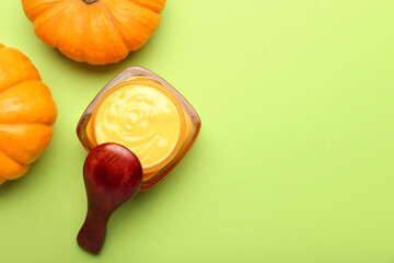 Jar of natural pumpkin mask and spoon on green background
