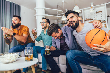 Happy friends or basketball fans watching basketball game on tv and celebrating victory at home.