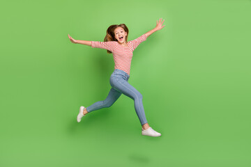 Fototapeta na wymiar Photo of excited crazy inspired lady jump run have fun raise hands wear striped shirt isolated green color background