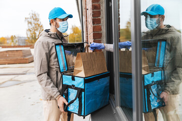 food shipping, pandemic and people concept - delivery man in mask with open thermal insulated bag giving order to customer at home