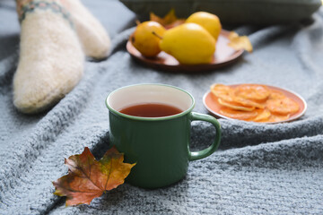 Green cup of hot tea and fallen leaf on grey fabric background, closeup
