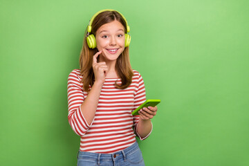 Photo of cheerful blogger lady hold phone listen song wear headphones striped shirt isolated green color background