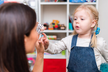 Woman speech therapist helps little girl to correct her speech in her office