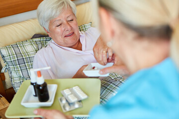 Elderly care worker distributes pills to sick elderly woman in bed