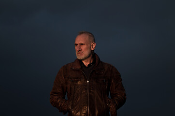 Portrait of adult man in brown leather jacket against blue sky during sunset