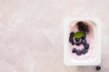 Fresh wild blueberries as an addition to yogurt. A standard portion of fruit yogurt in a plastic cup is covered with fresh blueberries. Top view. Copy space. 