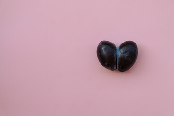 Two heart-shaped plums. Amaranth Pink Color background. Copy space. 