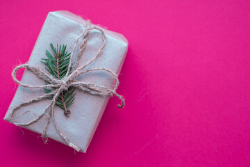 Eco friendly zero waste handmade Christmas gift box in craft reusable paper. Plastic free holidays. Stylish simple present with green fir branch on hot pink background. DIY, top view. Copy space.