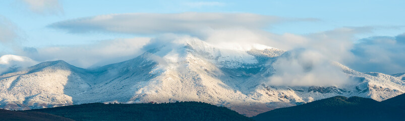 Stunning view of a snowcapped mountain range surrounded by fog and clouds