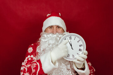 Santa is holding a white clock that says it's two minutes to twelve. close up