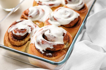 Baking dish of tasty cinnamon rolls with cream on light background, closeup