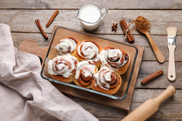 Baking dish of tasty cinnamon rolls with cream on wooden background