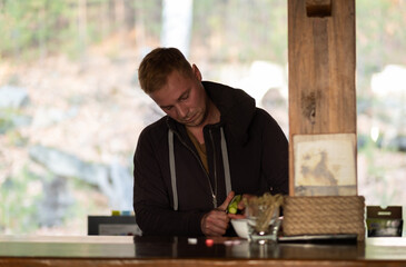 A young man is peeling a cucumber in the kitchen against the background of a large window